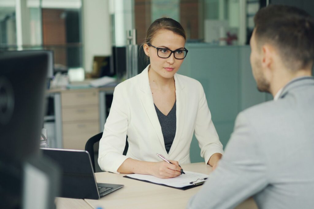 Employer Branding im Bewerbungsgespräch: Eine Frau mit Brille spricht mit einem Bewerber am Schreibtisch