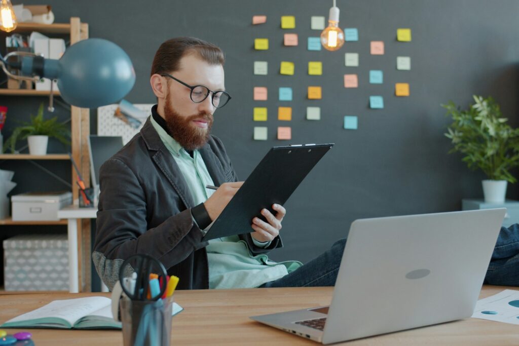 Serial Entrepreneur bei der Arbeit: Bärtiger Gründer am Schreibtisch mit Laptop und Unterlagen
