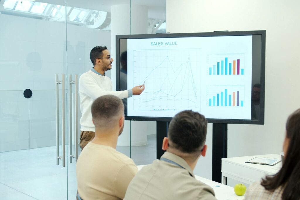 Strategie kommunizieren: Mann präsentiert Diagramme auf einer großen Leinwand vor Publikum