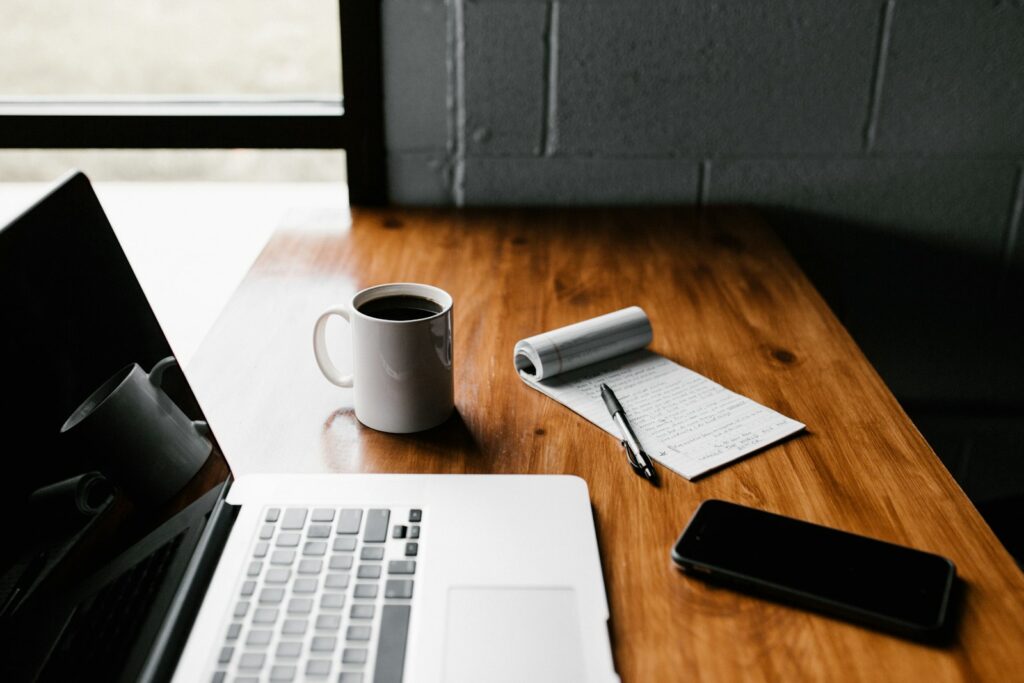 Laptop, Kaffee und Notizbuch auf einem Holztisch
