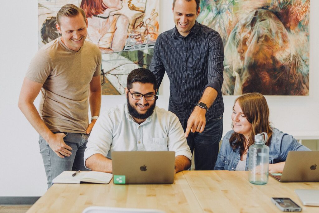 Vier junge Kollegen lachen gemeinsam vor einem Laptop – Generation Z im Team