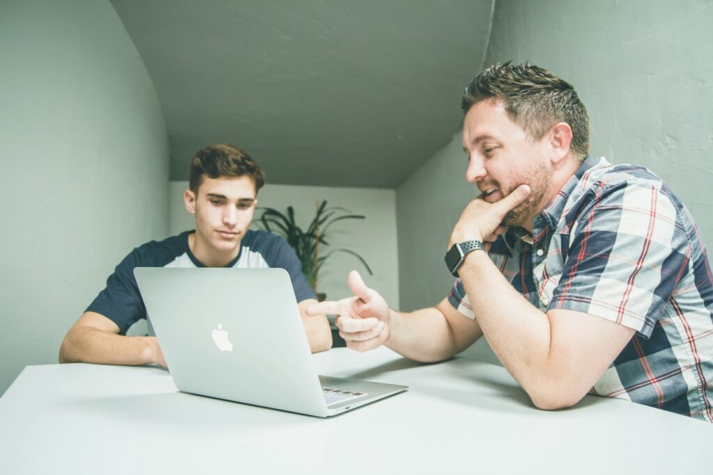 Erfahrener Kollege erklärt einem jüngeren etwas am Laptop – Mentoring für die Generation Z