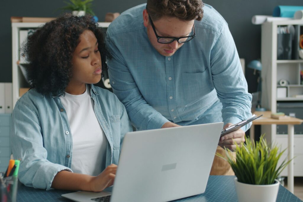 Zwei Kollegen arbeiten gemeinsam an einem Schreibtisch, wie ein Buddy im Remote Onboarding unterstützt
